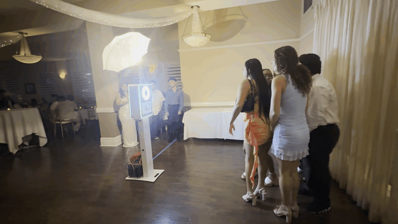 Self-serve digital photo booth centered between decorated dining tables at a graduation event venue.