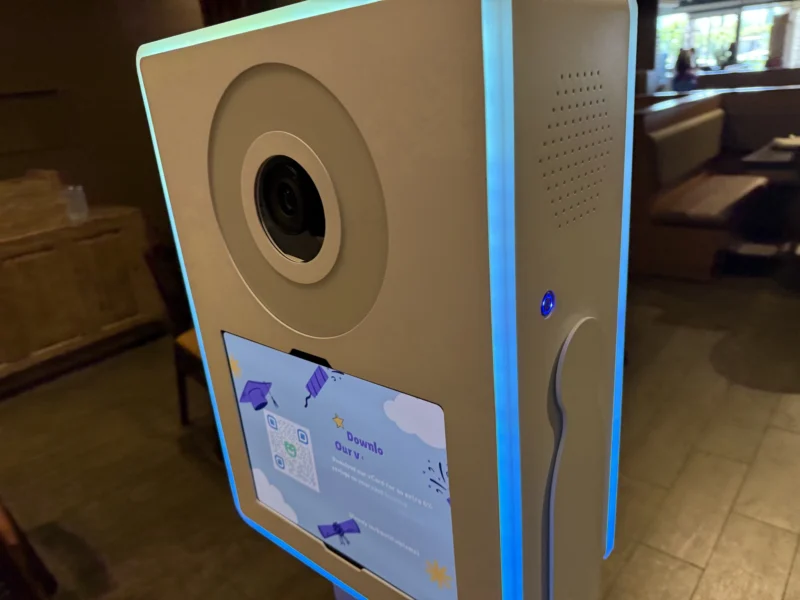 Close-up of a self-serve digital photo booth with glowing blue edge lighting and built-in sharing screen at an event venue.