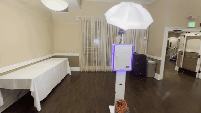 Self-serve digital photo booth centered inside an event dining space with round tables and graduation decor.