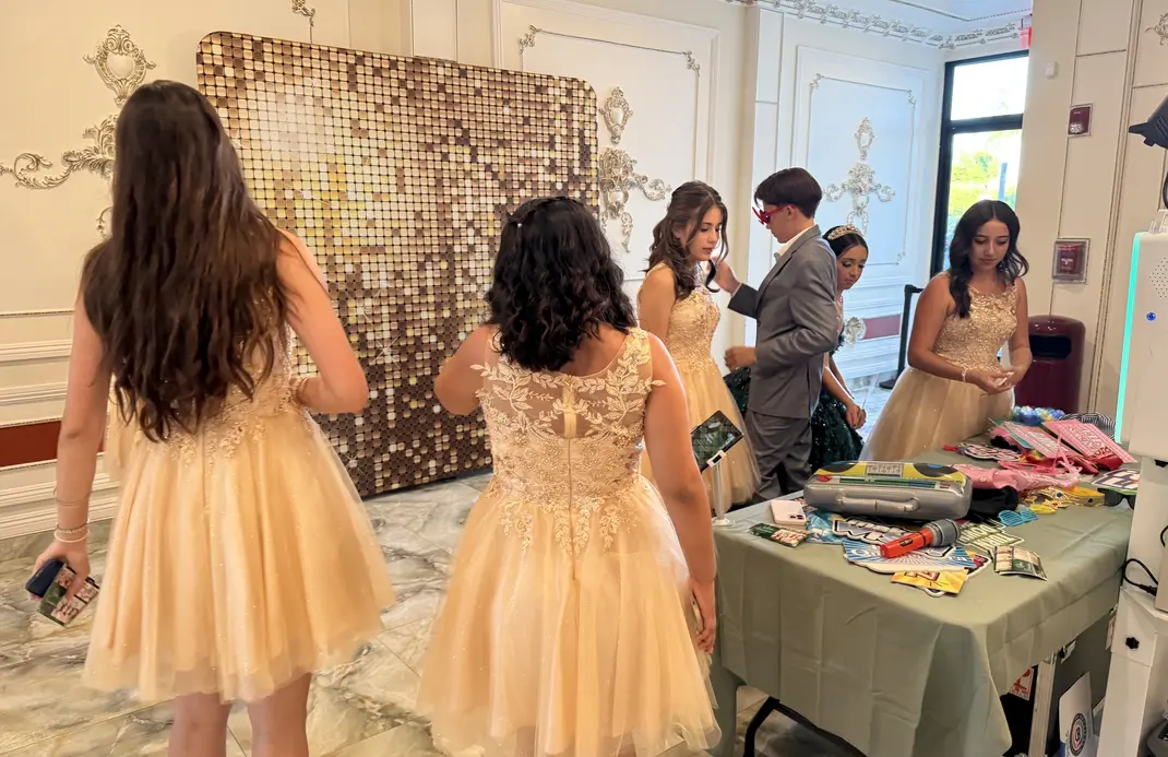 Event guests gathered near a photo booth with a gold sequin backdrop, showing a polished and complete booth setup for a celebration.