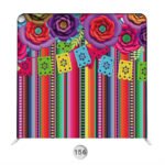 Colorful fiesta photo booth backdrop with serape stripes, papel picado banners, and oversized floral accents.