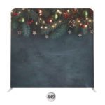 Holiday photo booth backdrop with evergreen garland, ornaments, berries, and warm string lights over a dark blue background.