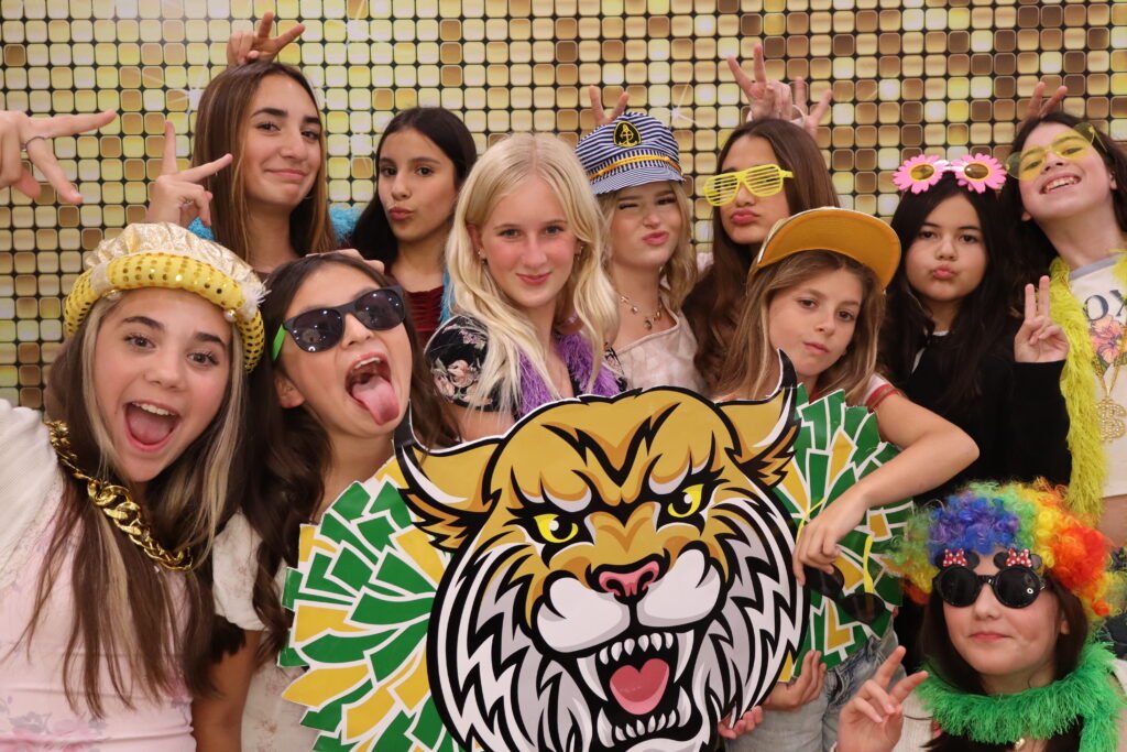 Kids and teens posing with props at a beÜtiful Pixels photo booth in front of a gold sequin backdrop