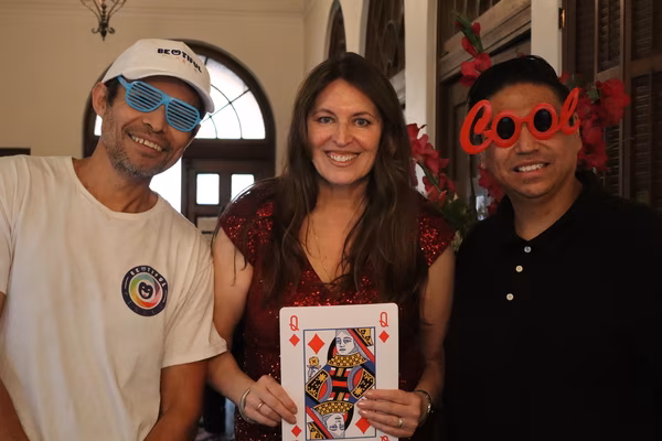 Three happy guests with a large Queen of Diamonds playing card and fun prop glasses at the Kings and Queens Royale Casino Fundraiser in Santa Ana, California.