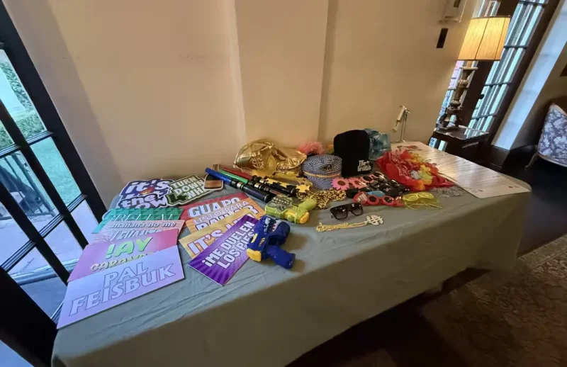 A table full of interactive photo booth props including bilingual Spanish signs, lightsabers, and colorful sunglasses for an Orange County event.