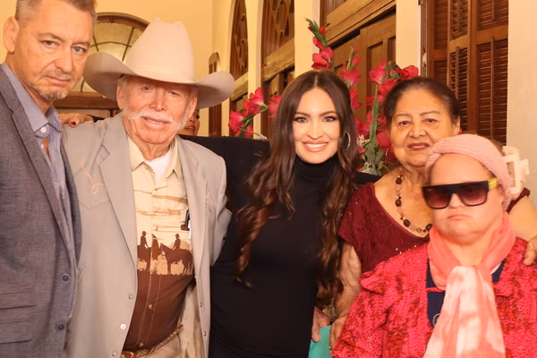 A group of five guests of varying ages posing for a portrait, featuring a man in a classic cowboy hat and a guest in the front wearing large dark sunglasses and a pink head wrap.