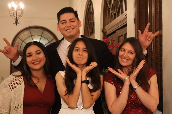 A smiling group of four people posing playfully together, with a man in the back making hand signs and two women in the front framing their smiling faces with their hands, at the Ebell Club in Santa Ana.